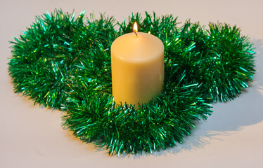 Burning Christmas candle with green tinsel