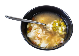soup with stelline (italian pasta) and vegetables (cauliflower, broccoli, etc) in black bowl with spoon isolated on white background