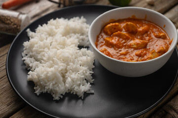 Close-up view of plate with delicious chicken tikka masala curry and rice on rustic wooden table with spices background. Traditional Indian dish. Exotic tasty meal. Appetizing photo for menu or recipe