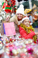 Fototapeta na wymiar Portrait of smiling teen girl with mother holding shopping bags with purchases on street Christmas market
