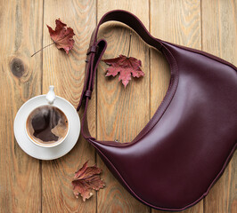 Leather bag, cup of coffee and autumn leaves on a wooden background