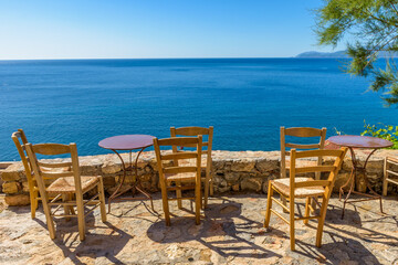 Obraz na płótnie Canvas Traditional cafe exterior in the fortified medieval castle of Monemvasia. Iron tables and wooden chairs with the view of the aegean sea in the background.