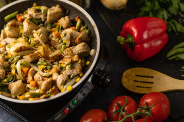Top view of pan with frying pork meat and mix of vegetables near ingredients on black background. Backstage of cooking dinner. Traditional italian dish. Concept of tasty food. Restaurant meal.