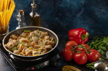 Top view of pan with frying pork meat and mix of vegetables near ingredients and cutlery on black background. Backstage of cooking dinner. Concept of tasty food. Restaurant meal.