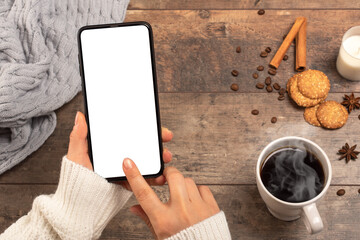 Mockup image of woman's hands holding mobile phone with blank white desktop screen while drinking coffee in cafe. cold weather, winter season