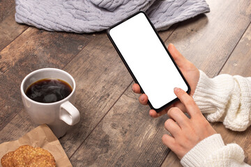 mockup image of woman's hands holding white mobile phone with blank screen on vintage wooden table background.