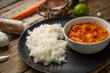 Tasty chicken curry with boiled rice on rustic wooden table with spices background. Dinner with traditional Indian dish. Exotic delicious. Food concept.