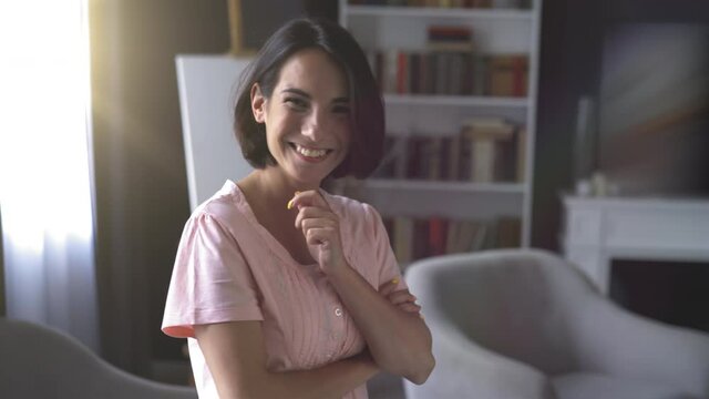 Smiling affably woman with short haircut. Her hands folded on chest against on living-room background. High quality 4k footage