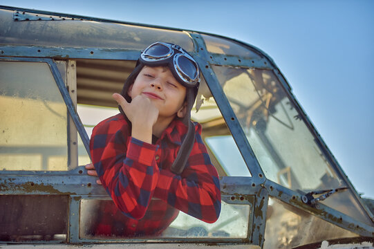 Portrait of a happy boy in a flying retro helmet in the cockpit of an old plane