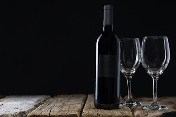 Elegant wine bottle and glasses stands on the rustic wooden table on black background. Space for...