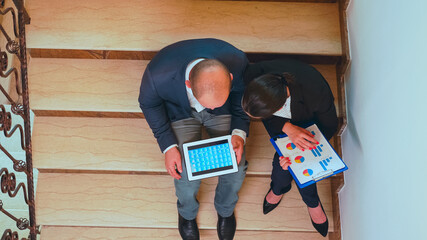 Top view of businesswoman holding clipboard discussing with company manager on stair of business building analysing reports. Group of professional businesspeople working in modern financial workplace.