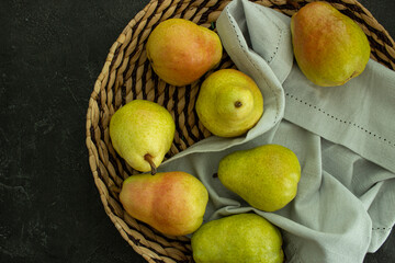 Fototapeta na wymiar Fresh pears in round straw plate on dark background