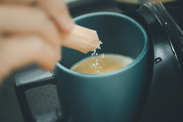 Hand pouring a sugar packet into a cup of coffee.