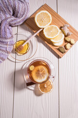 Warming vitamin tea with lemon and ginger in a glass Cup, sliced lemon and ginger on a cutting Board, white background. Vertical orientation.