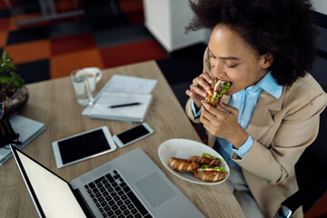 African American businesswoman eating sandwich on lunch break in the office.