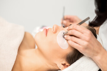 Obraz na płótnie Canvas Young caucasian woman having eyelash extension procedure in beauty salon. Beautician glues eyelashes with tweezers