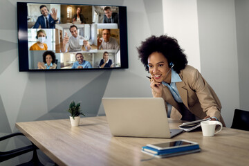 Happy black businesswoman using laptop while having conference call with her colleagues.