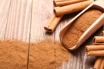 Scoop with cinnamon powder and sticks on wooden background, closeup