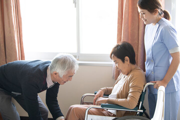 車椅子に乗ろうとする女性、支える夫と看護師