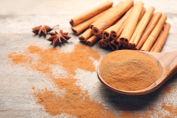 Spoon with cinnamon powder and sticks on wooden background, closeup