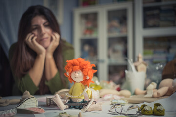 A young long-haired woman looks at her rag doll that she has created and finished