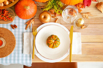 Beautiful table setting with pumpkins and autumn leaves in dining room