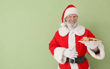 Santa Claus with tasty gingerbread cookies on color background