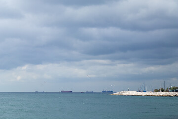 Fototapeta na wymiar Thunderclouds over the sea. Cargo ships at sea. Stone embankment