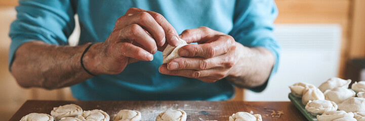 hands of senior man cooking and molding small homemade uncooked dumplings with meat on kitchen...