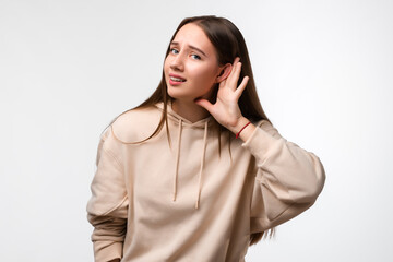 Young pretty brunette woman keeps palm of a hand close to ear as if listening to rumors