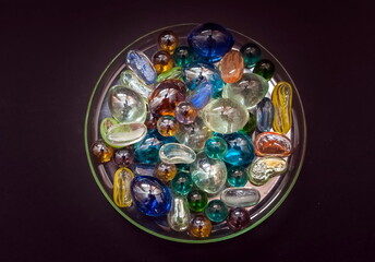 Glass colored decorative beads on a glass transparent saucer close up on a black background