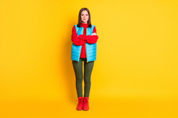 Fototapeta na wymiar Full length photo of cute lovely young lady smiling crossed hands self-assured look waiting wear green pants blue vest red sweater boots isolated bright yellow color background