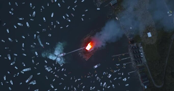 Extremely interesting, high altitude, turning aerial footage of small motor boats, sail boats gathering around and witnessing the biggest bonfire event on Earth at Alesund, Norway at dusk.