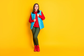 Full body size photo of charming lovely young lady beaming smiling wrapping warm clothes cold weather wear green pants blue vest red sweater boots isolated bright yellow color background