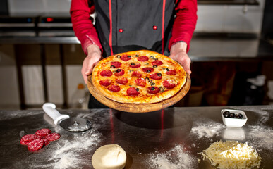 the hands of the chef are holding the cooked pizza