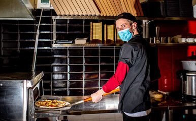 Cook Wearing a medical mask, put pizza in the oven for cooking