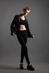 Obraz premium beautiful girl teenager in a black leather jacket and leggings posing in the studio on a gray background