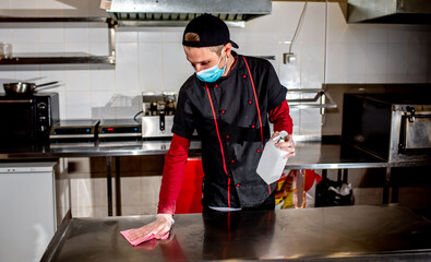 chef wearing medical mask disinfecting work table with antiseptic