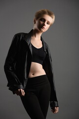 beautiful girl teenager in a black leather jacket and leggings posing in the studio on a gray background