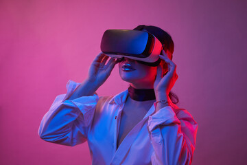 Woman with glasses of virtual reality in the neon lights. Girl in VR goggles having virtual reality...
