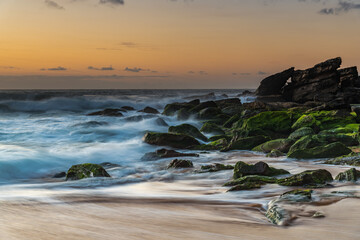 Sunrise seascape with light cloud, waves and rocks