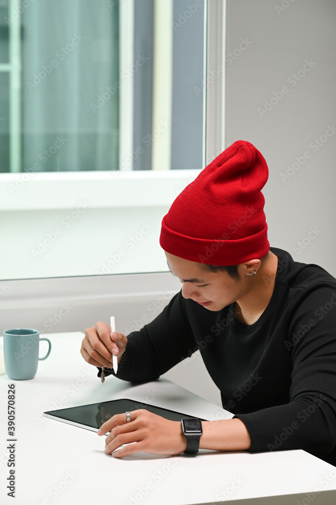 Poster portrait of a man graphic designer in red wool hat is using graphic tablet on his workspace.