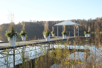 Moody landscape with wooden pier with white gazebo over a lake surrounded by forest in autumn...