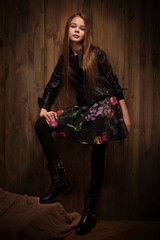 beautiful girl teenager in a leather jacket and colored skirt posing on a wooden background