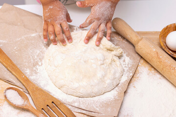 dough in flour kneading childrens hands, one kid, child helps parents in kitchen, concept of a happy childhood, household help, homework, food preparation