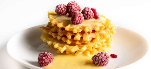 Weekend breakfast: waffles with condensed milk and raspberries. White background. Viennese waffles with condensed milk and raspberries on a white plate