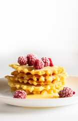 Weekend breakfast: waffles with condensed milk and raspberries. White background. Viennese waffles with condensed milk and raspberries on a white plate