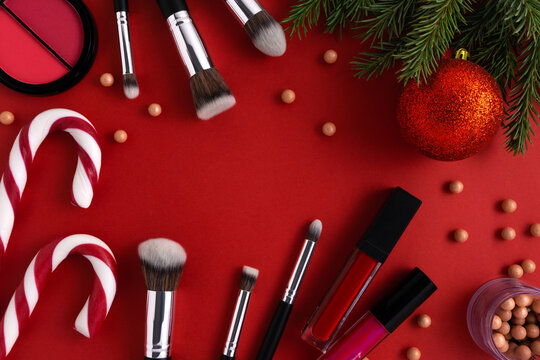 Creative concept fashion holiday christmas photo of cosmetics beauty products lipstick brushes and candy cane on red background.