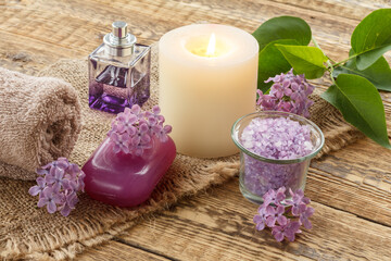 Towel, sea salt, candle and lilac flowers on wooden background.