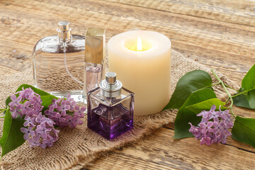 Obraz na płótnie Canvas Bottles of perfume, candle and lilac flowers on wooden background.